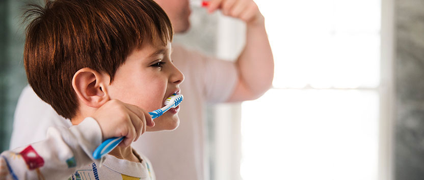 Boy brushing teeth alongside parent