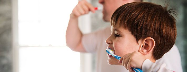 Boy brushing his teeth aside his parent