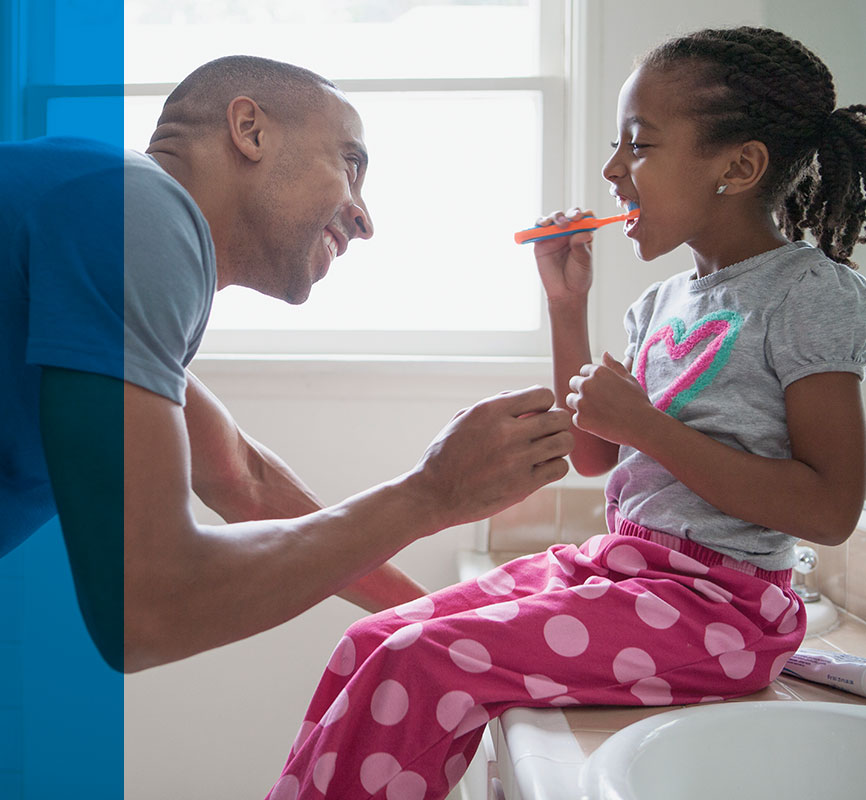 Daughter brushing teeth with father's playful supervision